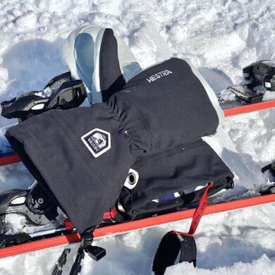 This photo shows the Hestra Army Leather Heli Ski Mitts outside on a pair of downhill skis on snow during the testing and review process.