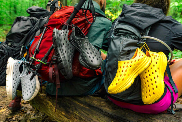 This photo shows the Kane Revive shoes attached to backpacks worn by hikers outside.