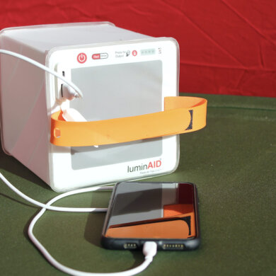 This photo shows the LuminAid PackLite Titan 2-in-1 Solar Lantern Charger charging a mobile phone on a camping cot in a tent.