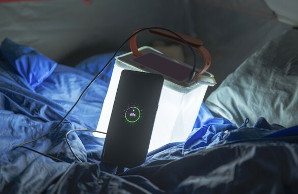 This photo shows the LuminAid PackLite Titan 2-in-1 Solar Lantern Charger turned on inside of a tent in the dark while charging a mobile phone.