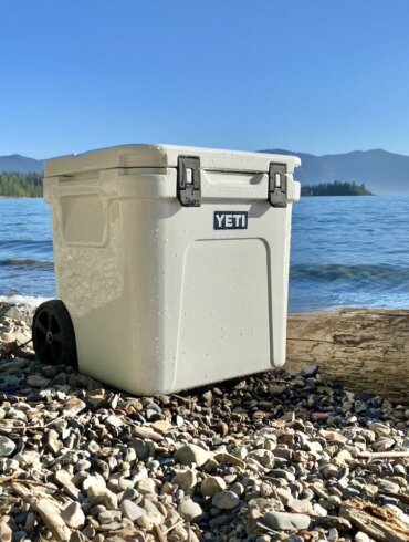 This best wheeled cooler testing and review photo shows a wheeled cooler on a beach next to a lake.