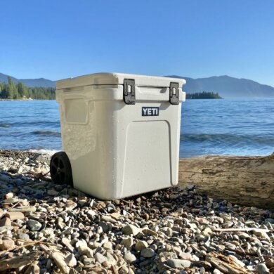 This best wheeled cooler testing and review photo shows a wheeled cooler on a beach next to a lake.