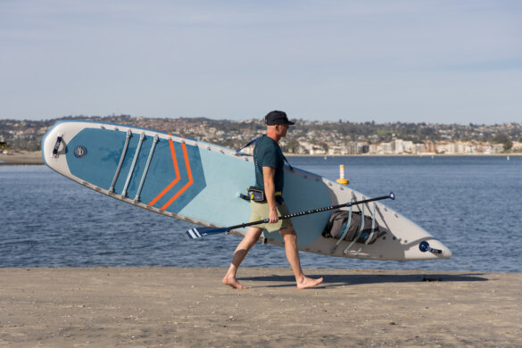 This photo shows a man carrying a new ISLE Explorer Pro iSUP on a beach.