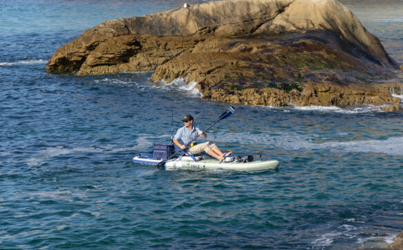 This photo shows a man using the ISLE Pioneer Pro iSUP in the kayak mode with fishing accessories and gear in an ocean.