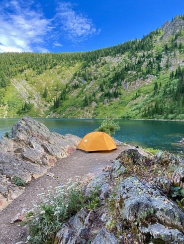 This photo shows a REI tent setup near a mountain lake.