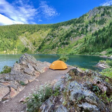 This photo shows a REI tent setup near a mountain lake.