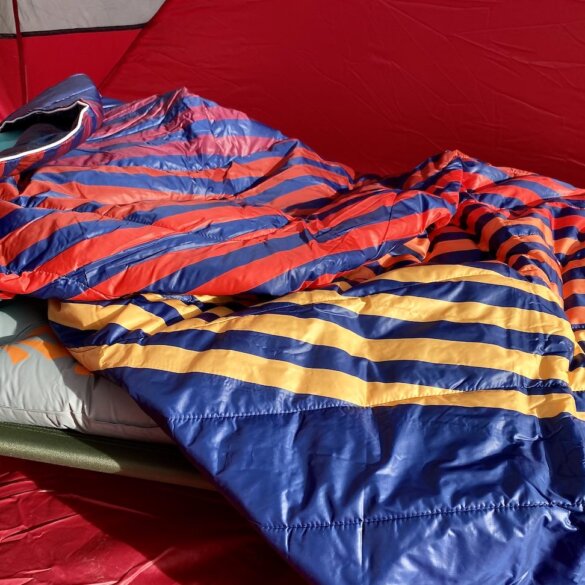 This testing and review photo shows the Rumpl Original Puffy Blanket inside a camping tent on an air mattress and camp cot.