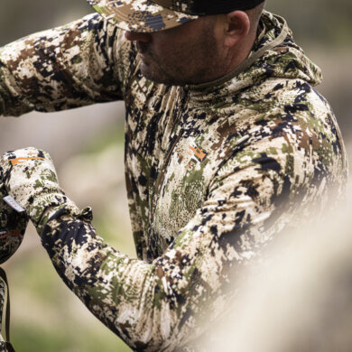This photo shows a hunter wearing Sitka's new Core Merino 120 Hoody while organizing gear in a Sitka hunting backpack.