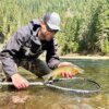 The author wearing the Smith Guide's Choice sunglasses while holding a cutthroat trout over a fly fishing net in a river.