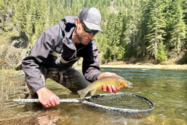 The author wearing the Smith Guide's Choice sunglasses while holding a cutthroat trout over a fly fishing net in a river.