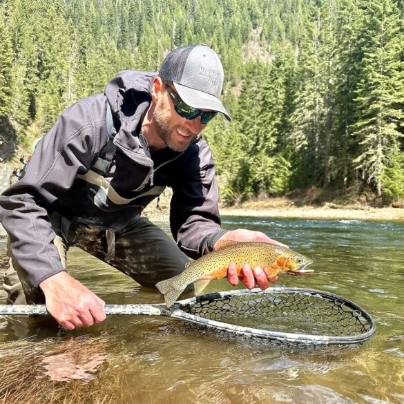 The author wearing the Smith Guide's Choice sunglasses while holding a cutthroat trout over a fly fishing net in a river.
