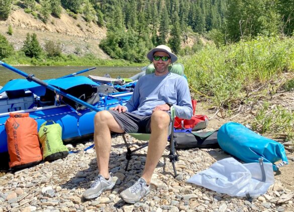 This photo shows the author sitting in the Cascade Mountain Tech Hammock Chair near a river during the testing and camping chair review process.