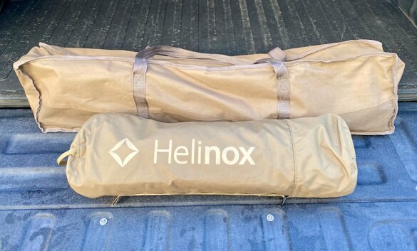 This photo shows the Helinox Cot One Convertible in its included travel bag next to a larger classic cot to show a size comparison.