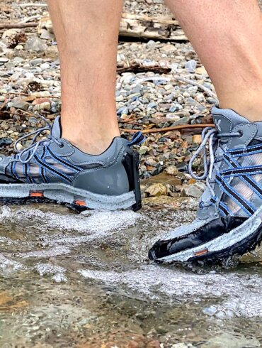 This review photo shows the author testing the men's Korkers All Axis Shoe in the water on a rocky shore.