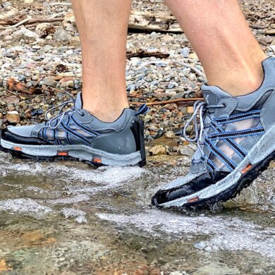 This review photo shows the author testing the men's Korkers All Axis Shoe in the water on a rocky shore.