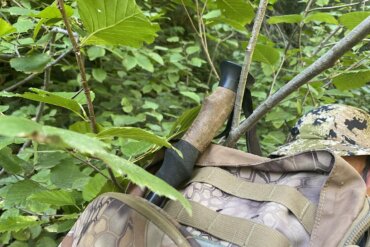 This photo shows telescoping style trekking poles attached to a hunting backpack getting caught on a branch in a forest.