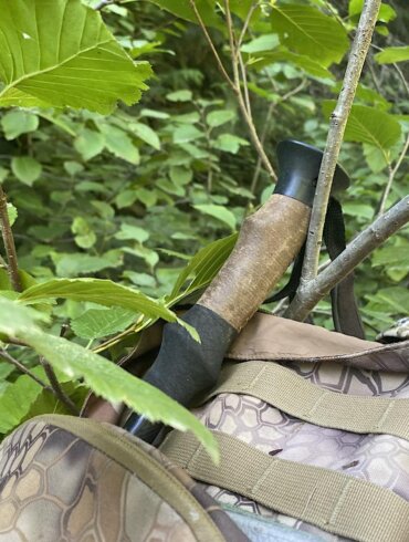 This photo shows telescoping style trekking poles attached to a hunting backpack getting caught on a branch in a forest.