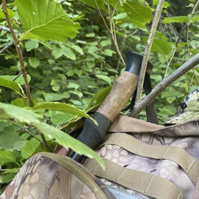 This photo shows telescoping style trekking poles attached to a hunting backpack getting caught on a branch in a forest.