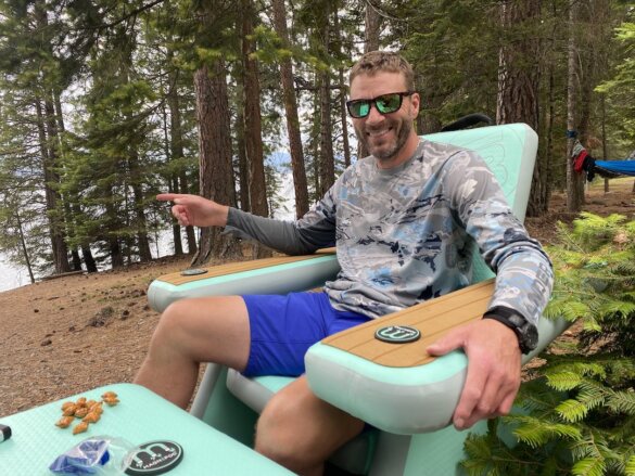 This photo shows the author sitting in the BOTE Inflatable AeroRondak Chair at a campsite near a lake.