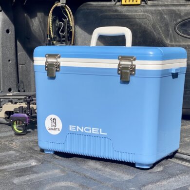 This review photo shows the Engel 19 Quart Drybox/Cooler on the tailgate of a pickup truck out in a forest during the real-world testing process.