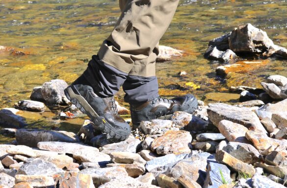 This review photo shows the author wearing the Grundens Bankside Wading Boots on a rocky shore near a river.