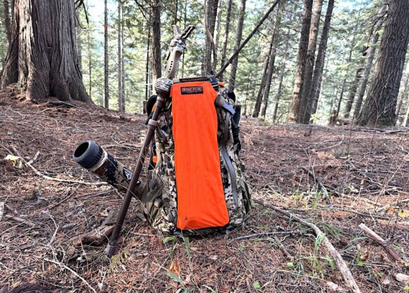 This hunting gift idea shows the Orange Aglow Safety Panel attacked to a camouflage hunting backpack in a forest.