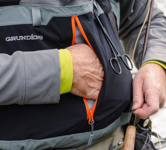This photo shows a close-up of the new Grundens Bedrock Stockingfoot Waders worn by a man who is showing the vertical chest pocket design feature.