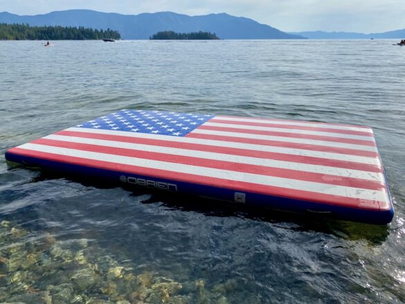 This review photo shows the O'Brien Runway Flag Edition Inflatable Float swim dock floating on a mountain lake.