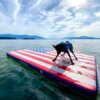 This review photo shows a dog standing on the O'Brien Runway Flag Edition Inflatable Float swim dock on a lake.