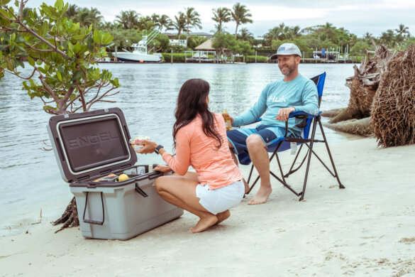 Man and woman with Engel 60QT Ultra-Light Injection-Molded Cooler on a beach near water.