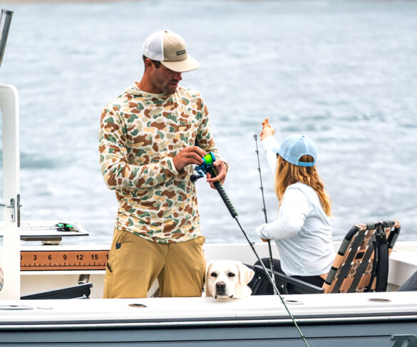 Man on a boat with fishing rod wearing Free Fly Vintage Camo Bamboo Lightweight Hoodie.
