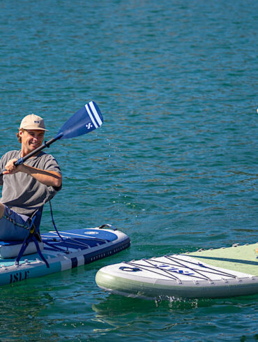 Man and woman each paddling on a new ISLE Pioneer 3 inflatable standup paddle board on a lake.