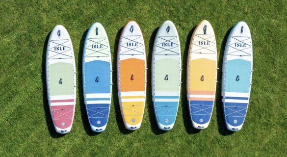 Six inflated ISLE Pioneer 3 standup paddle boards laying side-by-side on green grass to show the new color options.