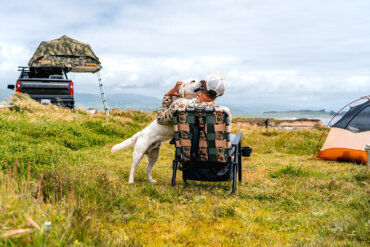 Man sitting in a camp chair in an off-grid camping location with a dog.