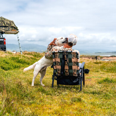 Man sitting in a camp chair in an off-grid camping location with a dog.