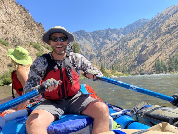 Author wearing Shelta hat rows a whitewater raft on a river.