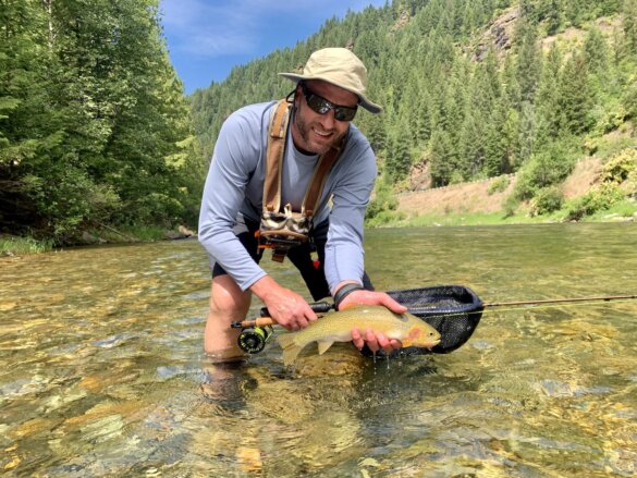 This shows the author wearing a Shelta Firebird V2 sun hat while fly fishing in a river.