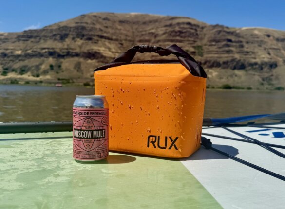 RUX Cooler Cube next to cold drink can on top of iSUP paddleboard near a beach. 