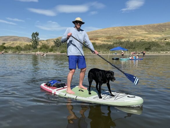Author standing on iSUP paddling on a lake with dog on front of iSUP.