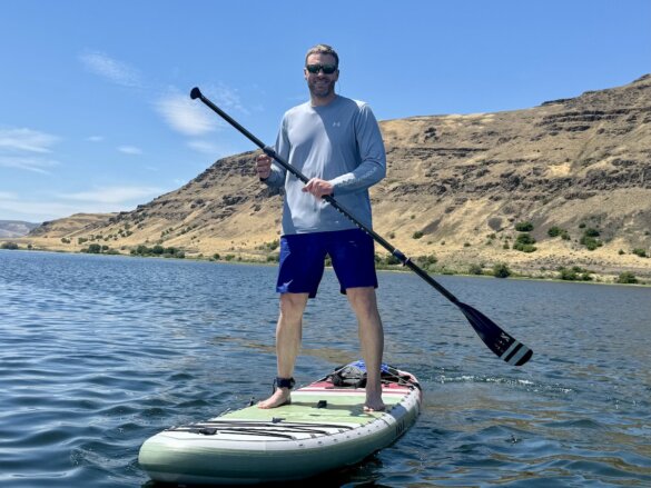 Author Chris Maxcer stands on the Pioneer iSUP while paddling on a lake.