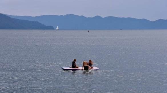 Three teenagers play on an inflatable swim dock that is floating on a mountain lake.
