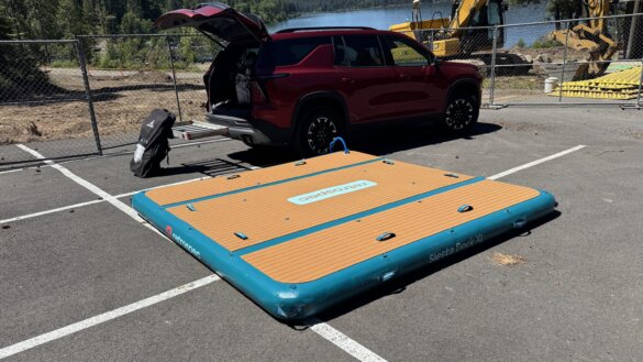 The Retrospec Siesta Dock XL Inflatable Platform 10' partially inflated in a beach site parking lot next to a vehicle.