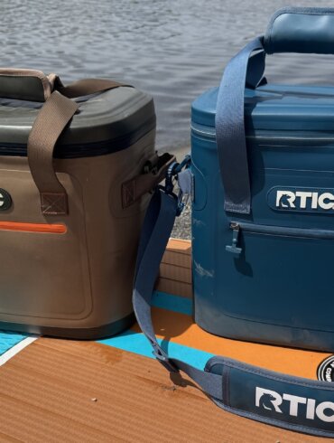 The RTIC 30-can and 20-can Ultra-Tough Soft Cooler side-by-side on an iSUP paddleboard on a beach near water.