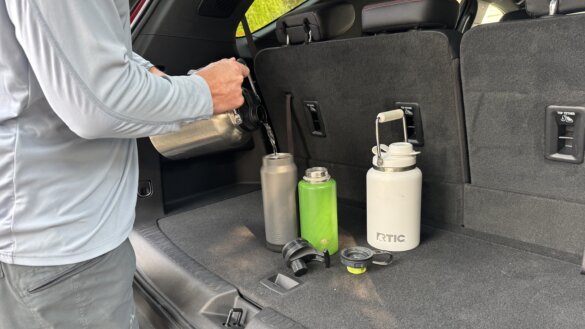 The author pours water from one Outback Jug into smaller water bottles sitting in the back of an SUV on a summer day.