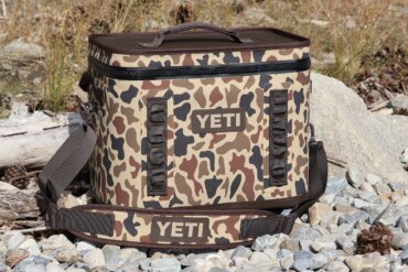 A YETI Hopper Flip 28 Soft Cooler on a rocky lake shore.